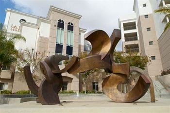 A large, abstract, metallic sculpture sits in front of a building
